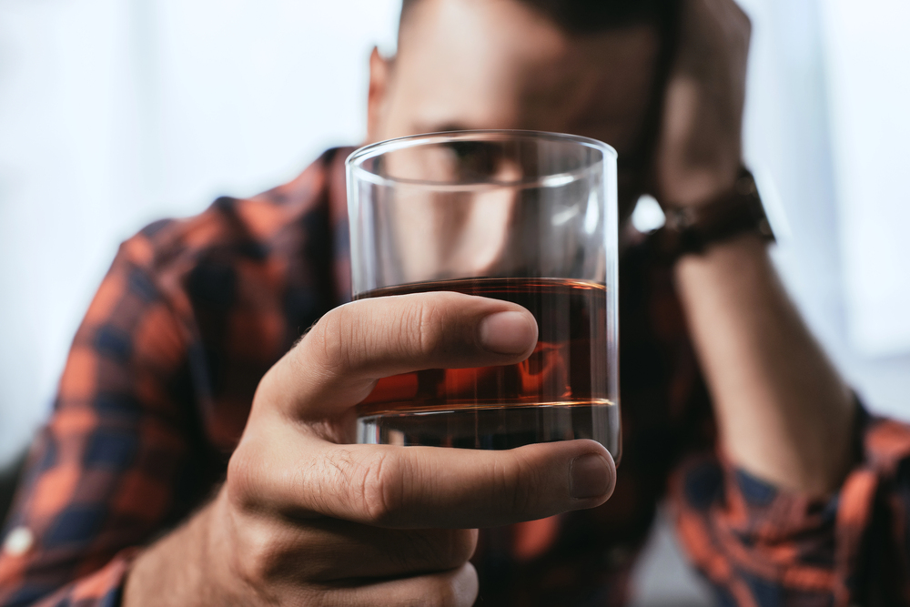 man holding a drink suffering from alcohol addiction