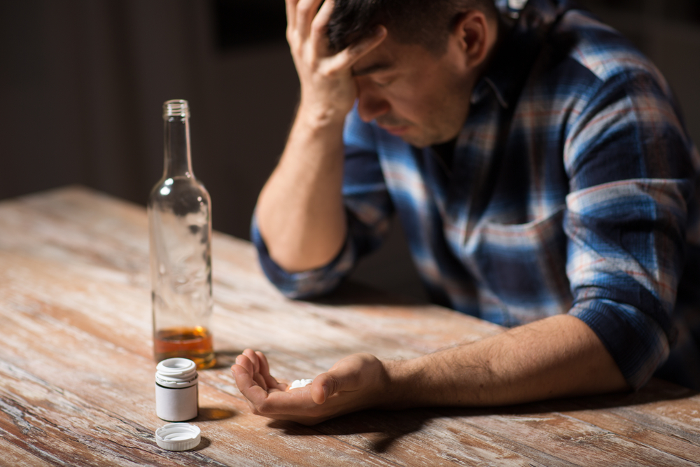 depressed drunk man with bottle of alcohol and pills