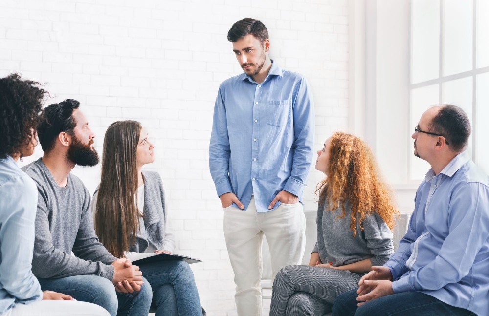 man in the middle of a group sharing experiences and progress of his recovery process