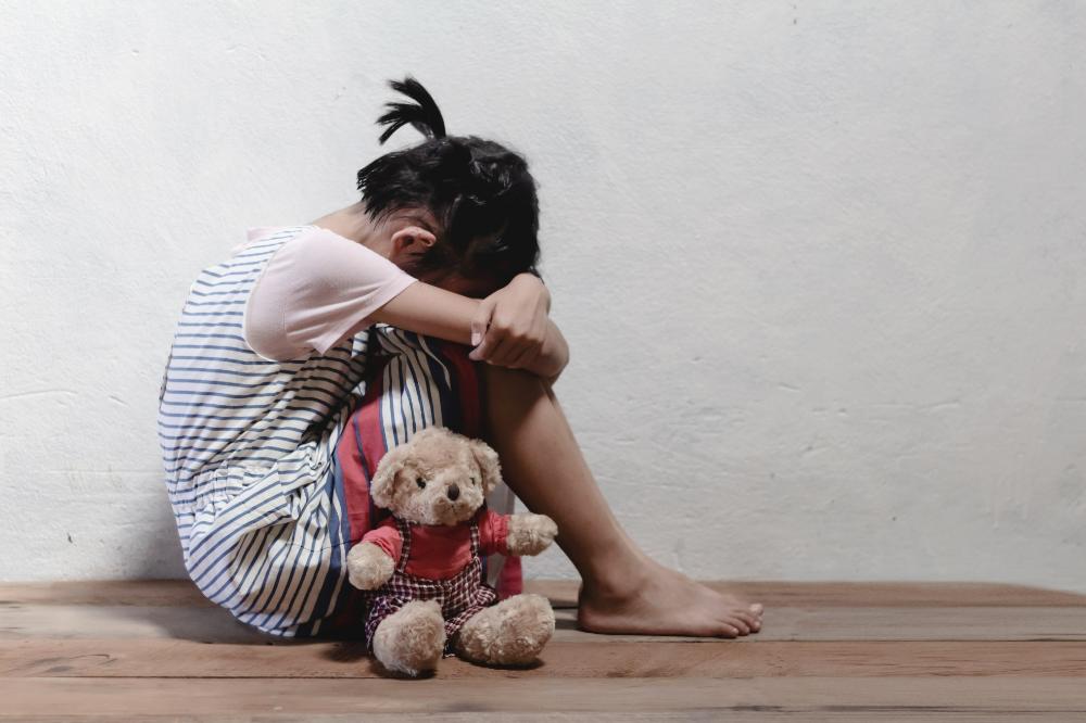 picture of a sad young little girl with here teddy on the floor