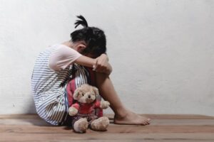 picture of a sad young little girl with here teddy on the floor