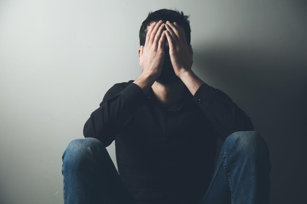 a picture of a man sitting on the floor with back leaning against the wall showing signs of depression, frustrations and regrets