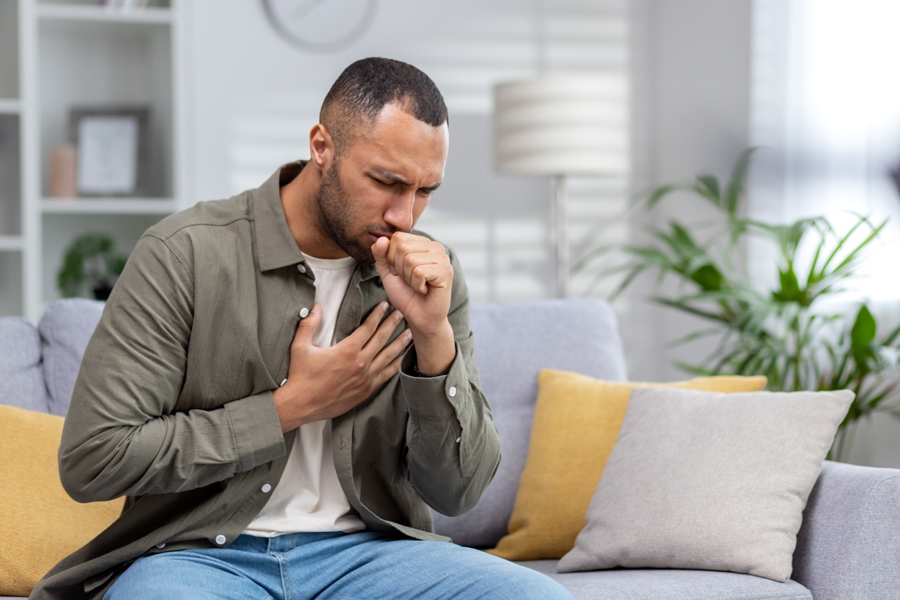 a young man sitting on the couch at home and coughing