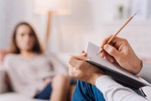 Therapist is taking note on a journal writing patients progress to her recovery