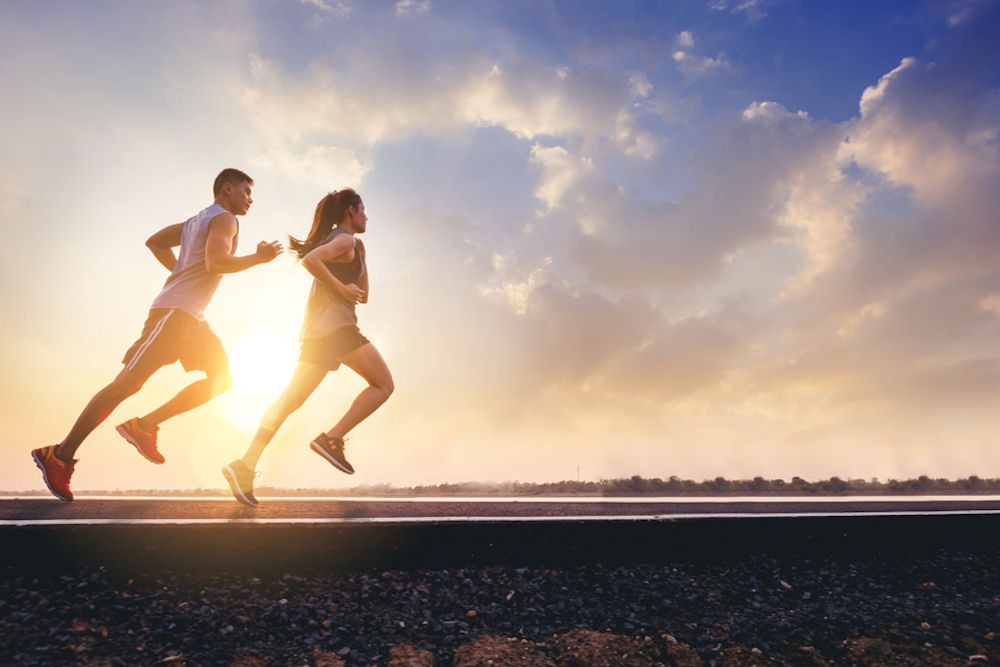 Man and woman running on track against distant sunset